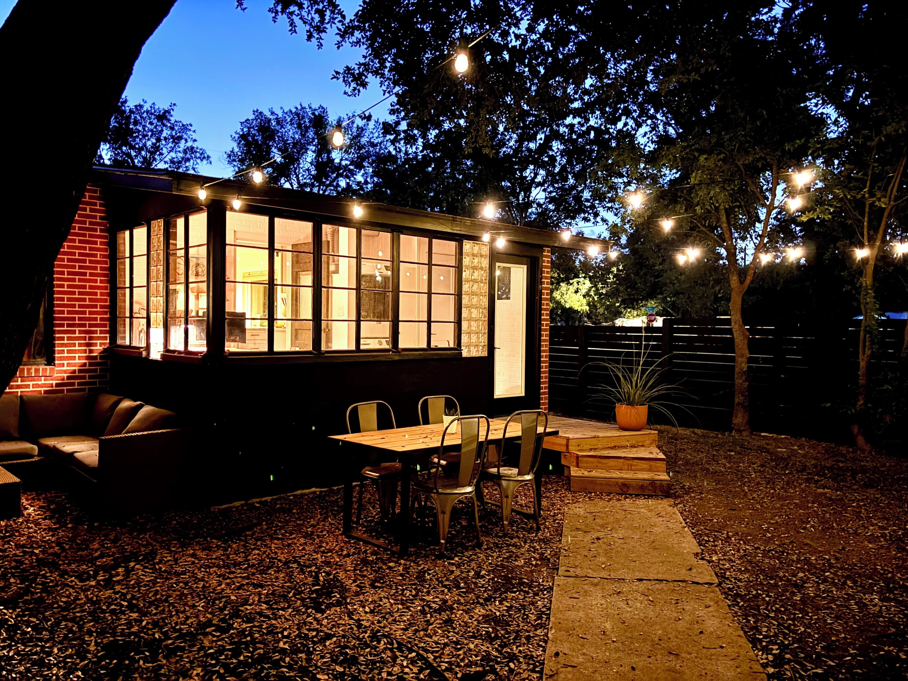 A cozy outdoor seating area with a table and chairs, surrounded by trees and a brick wall.
