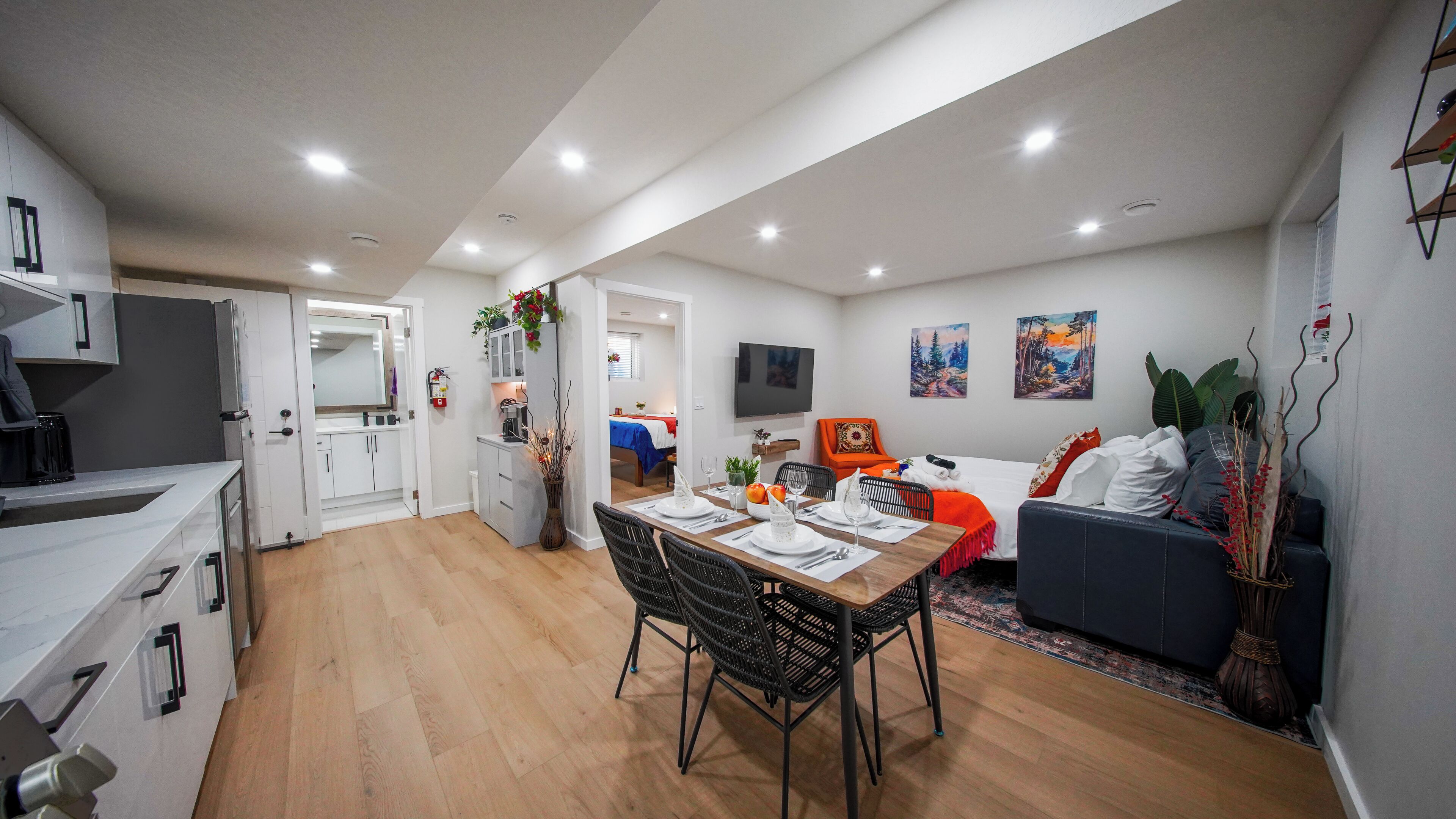 A modern apartment with a dining area, kitchen, living room, and a TV mounted on the wall.