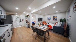 A modern apartment with a dining area, kitchen, living room, and a TV mounted on the wall.