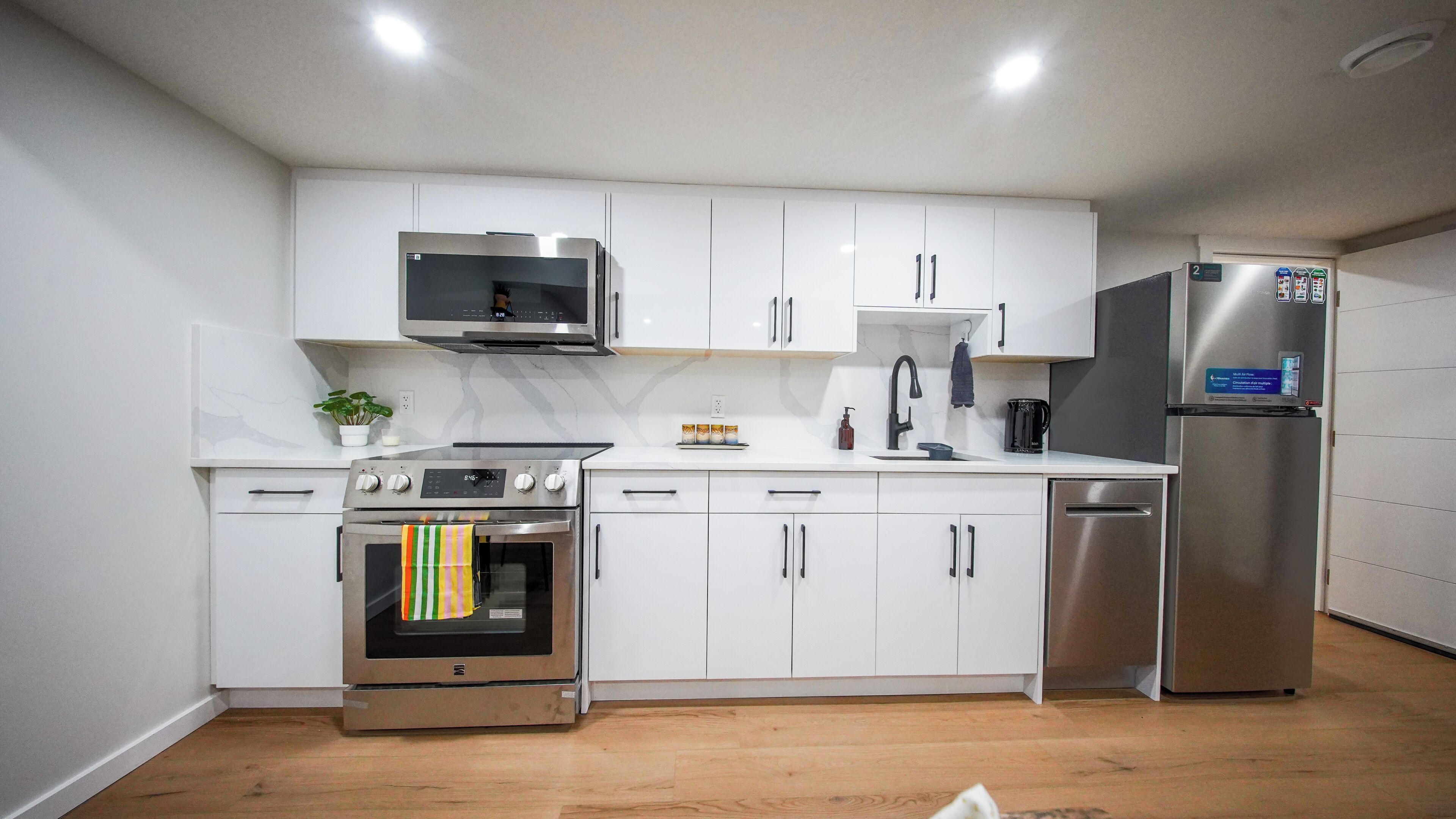 Una cocina moderna con armarios blancos, electrodomésticos de acero inoxidable y piso de madera.
