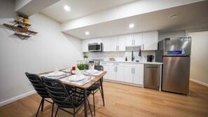 A modern kitchen with white cabinets, a stainless steel refrigerator, a microwave, and a dining area with a wooden table and black chairs.