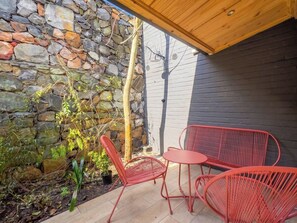 Eine Terrasse mit roten Metallstühlen und einem Tisch, eine Steinmauer und eine Holzbalkendecke.