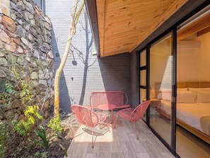 En moderne udendørs terrasse med en stenvæg, et træloft og en glasdør, der fører til et soveværelse.