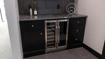 A kitchen with black cabinets, a stainless steel refrigerator, and a wine bottle on the counter.