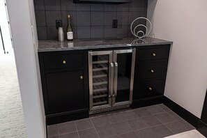 Une cuisine avec des meubles de couleur noire, un réfrigérateur en acier inoxydable et une bouteille de vin posée sur le comptoir.