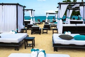 Ein Hotelzimmer am Strand mit mehreren Betten, jedes mit weißer Bettwäsche und blauen Akzenten, und Blick aufs Meer.