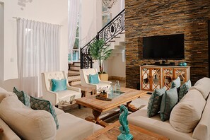 Ein Wohnzimmer mit einer Sofagarnitur, einem Couchtisch, einem Fernseher und einer Treppe mit Geländer.