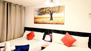 Habitación de hotel con cama, un cuadro de un árbol, una araña y una ventana con cortinas.