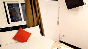 Una habitación de hotel con cama, ventana con cortinas, televisor montado en la pared y una toalla en el suelo.