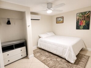 A bedroom with a bed, a wardrobe, a ceiling fan, an air conditioning unit, and a patterned rug.
