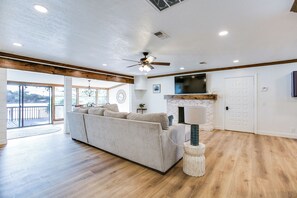 A spacious living room with a large sofa, a fireplace, a ceiling fan, and a television mounted on the wall. - Lakeside Home w/Private Casita & Stunning Views (San Angelo)
