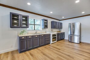 A modern kitchen with dark cabinets, a stainless steel refrigerator, and a window providing natural light. - Lakeside Home w/Private Casita & Stunning Views (San Angelo)