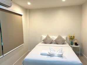 A hotel room with a bed, pillows, a towel, a nightstand, a lamp, and a vase with flowers. - 3-bedroom house in adorable Chalong Phuket with nestled among lush mature trees (Tambon Chalong)