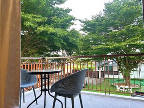 A balcony with two chairs and a table, a metal railing, and a view of a green lawn and trees. - 3-bedroom house in adorable Chalong Phuket with nestled among lush mature trees (Tambon Chalong)