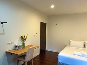 Ein Hotelzimmer mit einem Holztisch, einem Stuhl, einem Bett mit weißer Bettwäsche und einer Tür.