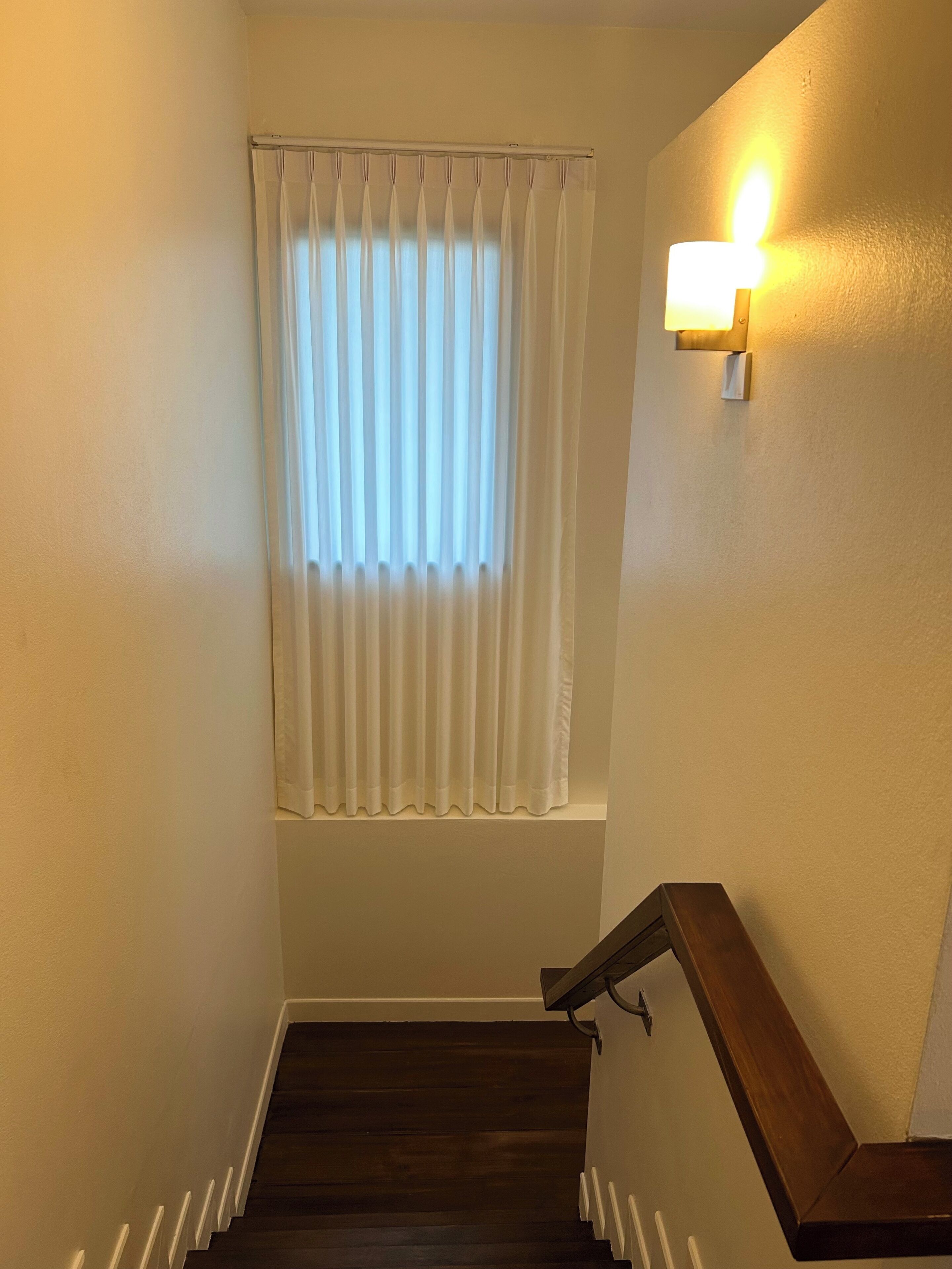 A staircase with a wooden handrail and a window with white curtains.