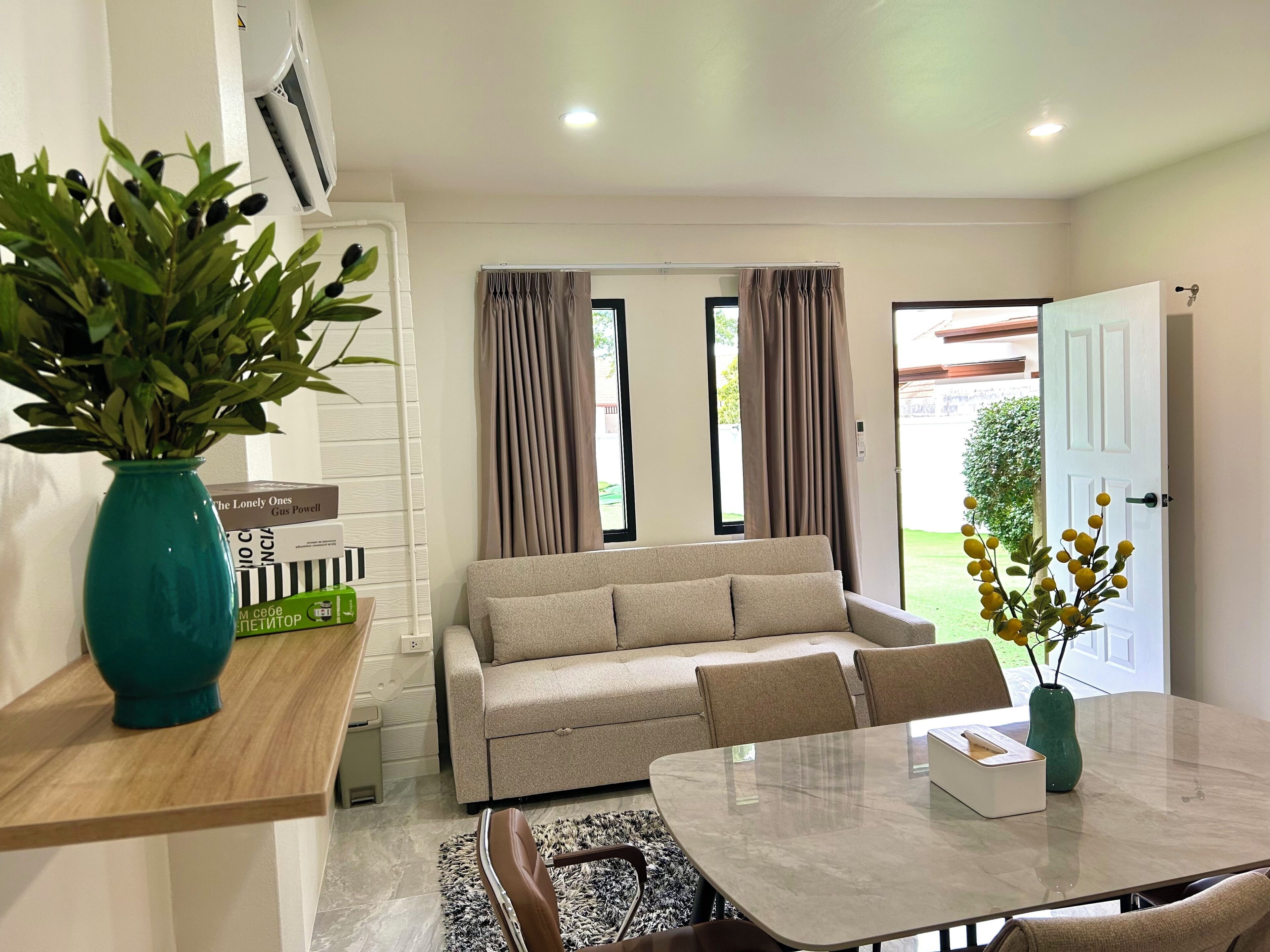 Un salon moderne avec un canapé, une table à manger et une table basse. Il y a une plante sur le côté gauche et une fenêtre avec des rideaux.