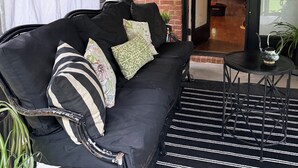 Un canapé noir avec des coussins à motifs, une petite table ronde avec une théière, et un tapis rayé noir et blanc.