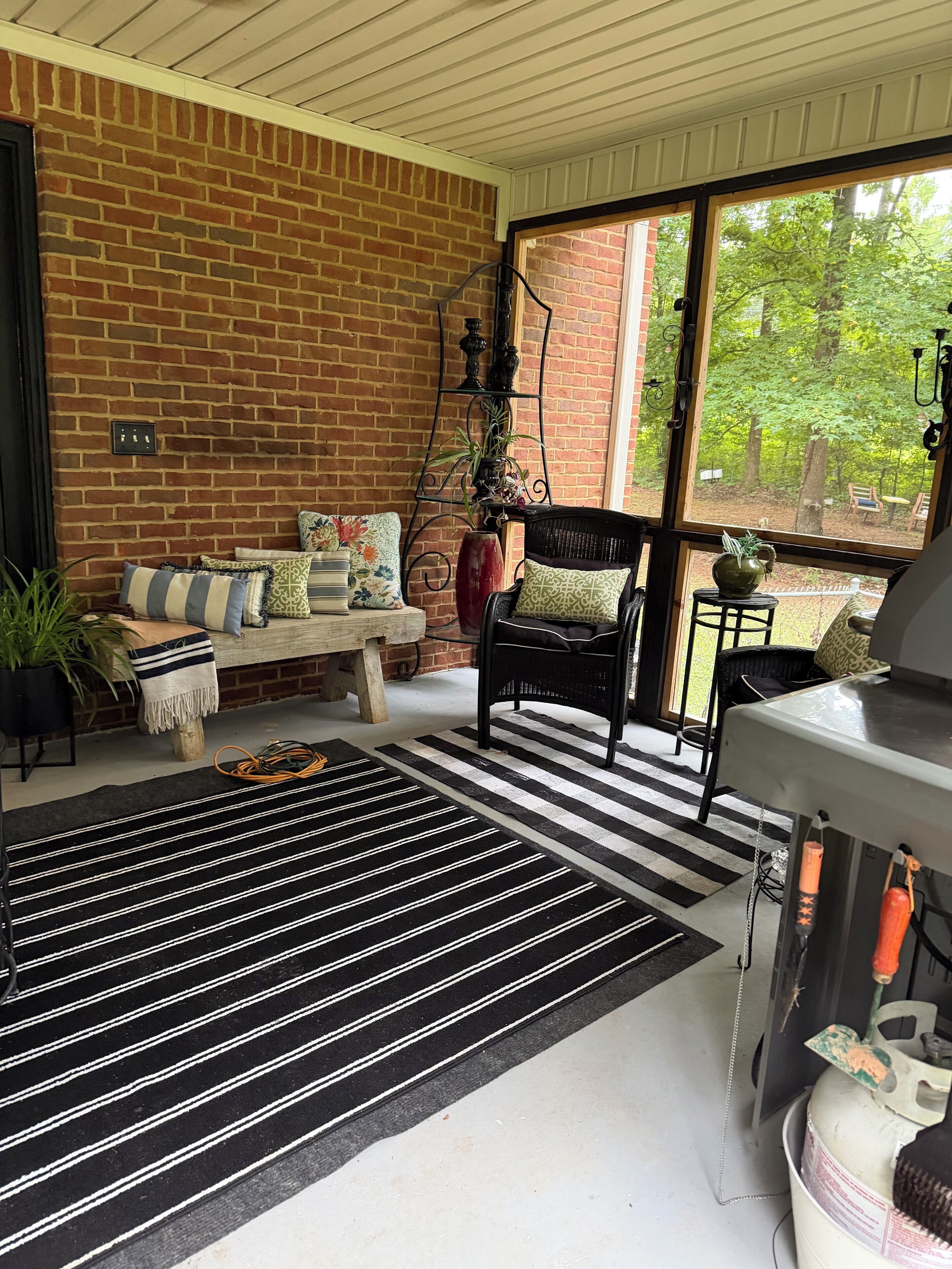 Una habitación acogedora con pared de ladrillo, un tapete a rayas blanco y negro, una silla negra y una mesa con una parrilla.