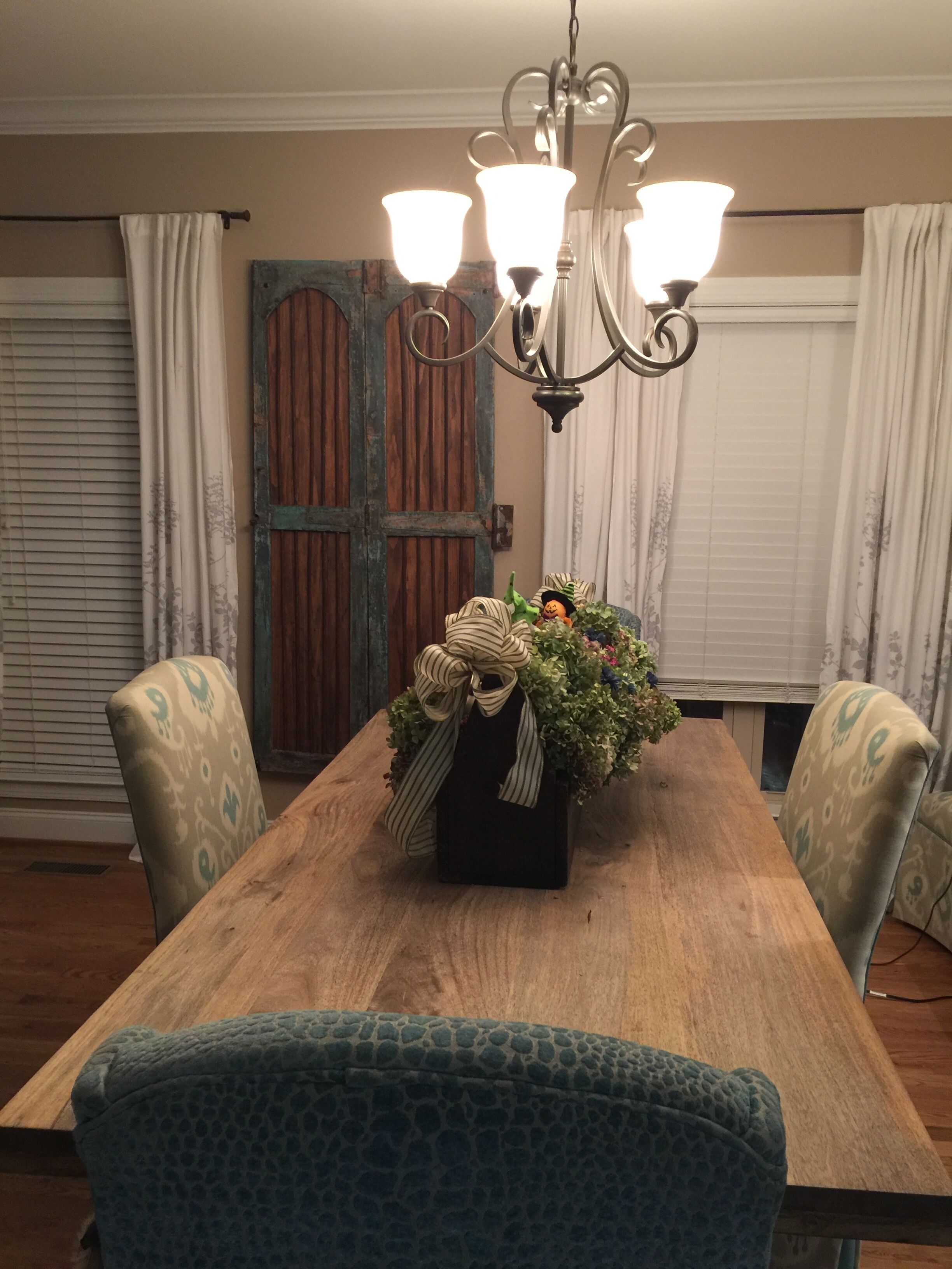 A dining table with a floral centerpiece, two chairs with patterned upholstery, and a chandelier with multiple light fixtures.