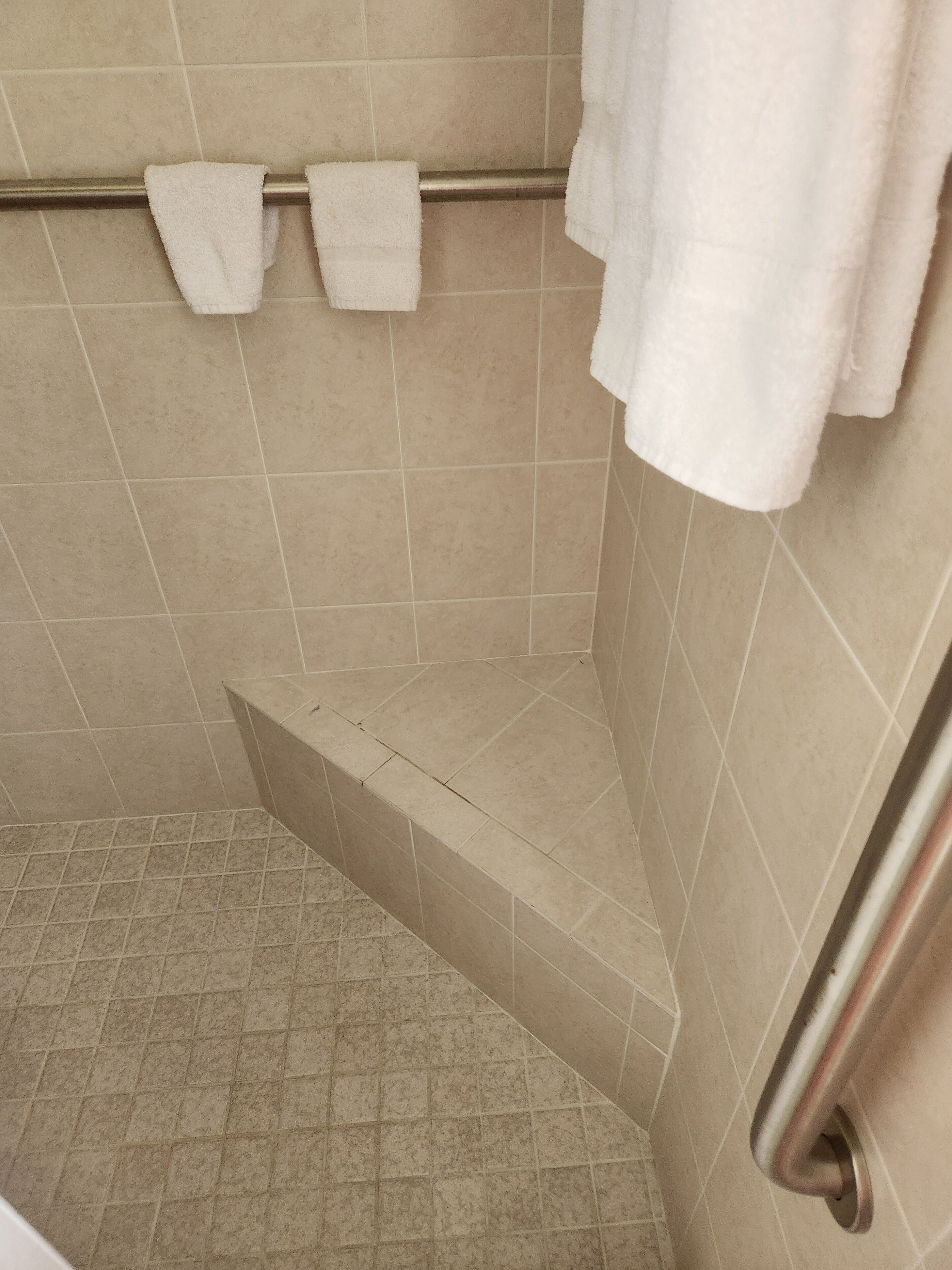 A corner of a bathroom with beige tiles, a metal towel rack, and a shower seat.