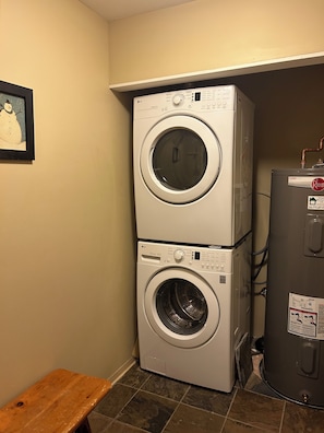 A laundry room with two stacked front-loading washing machines and a water heater. - Ski in Ski out condo in Whistler. Just a 3 minute walk from the upper village. (Whistler)