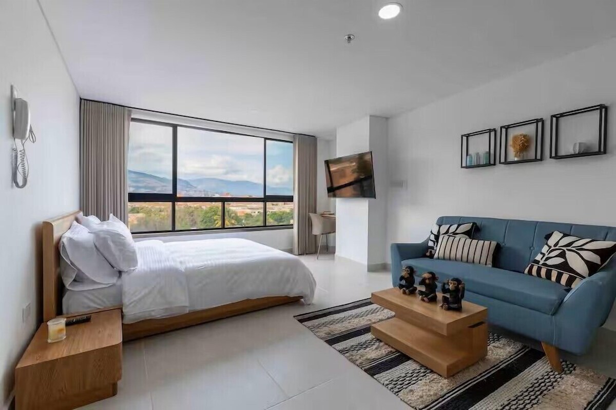A modern hotel room with a large bed, a sofa, a coffee table, and a TV mounted on the wall.