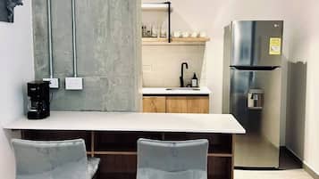 A modern kitchen with a bar area, stainless steel appliances, and a concrete accent wall.