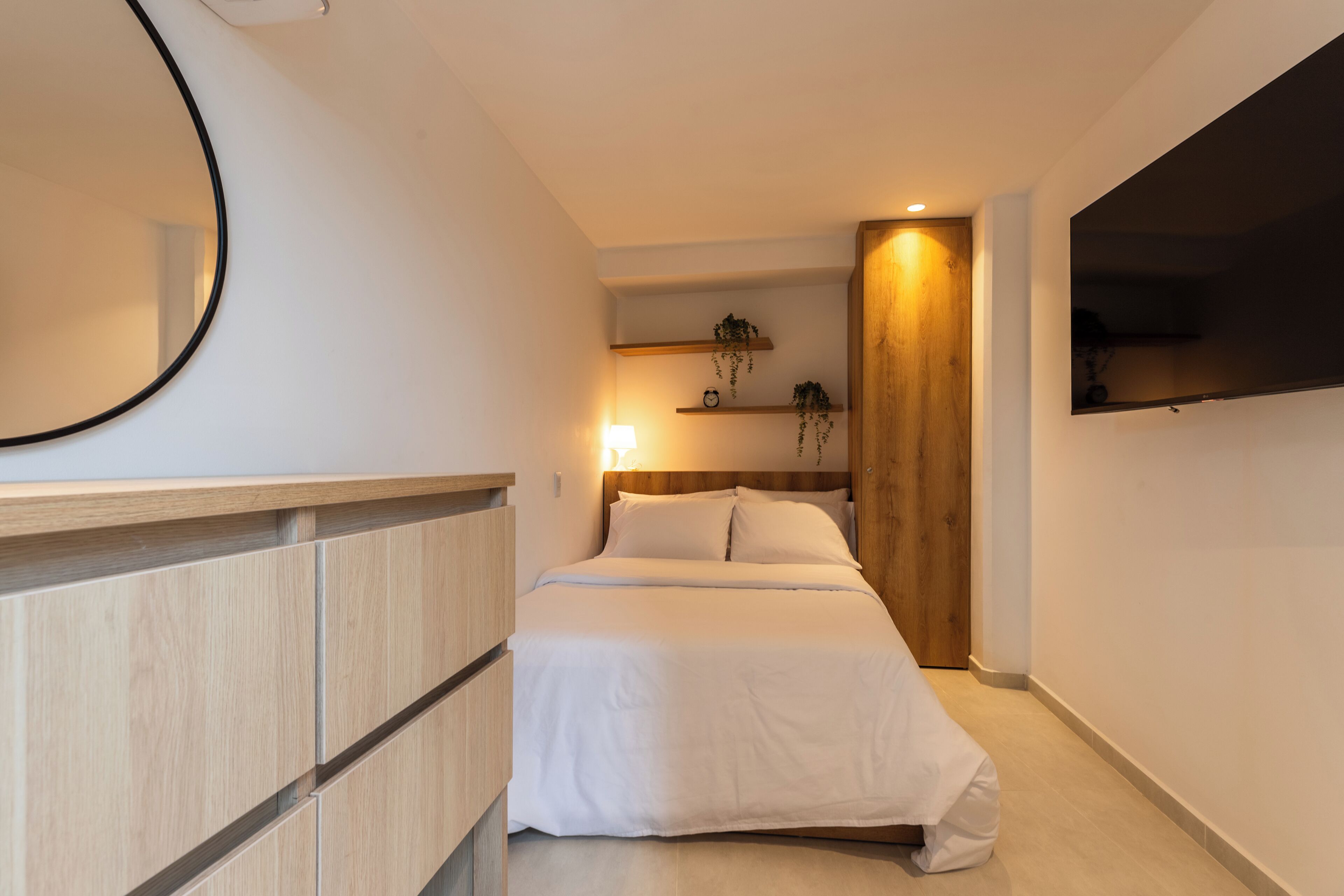 A modern bedroom with a bed, bedside table, and a wall-mounted TV.