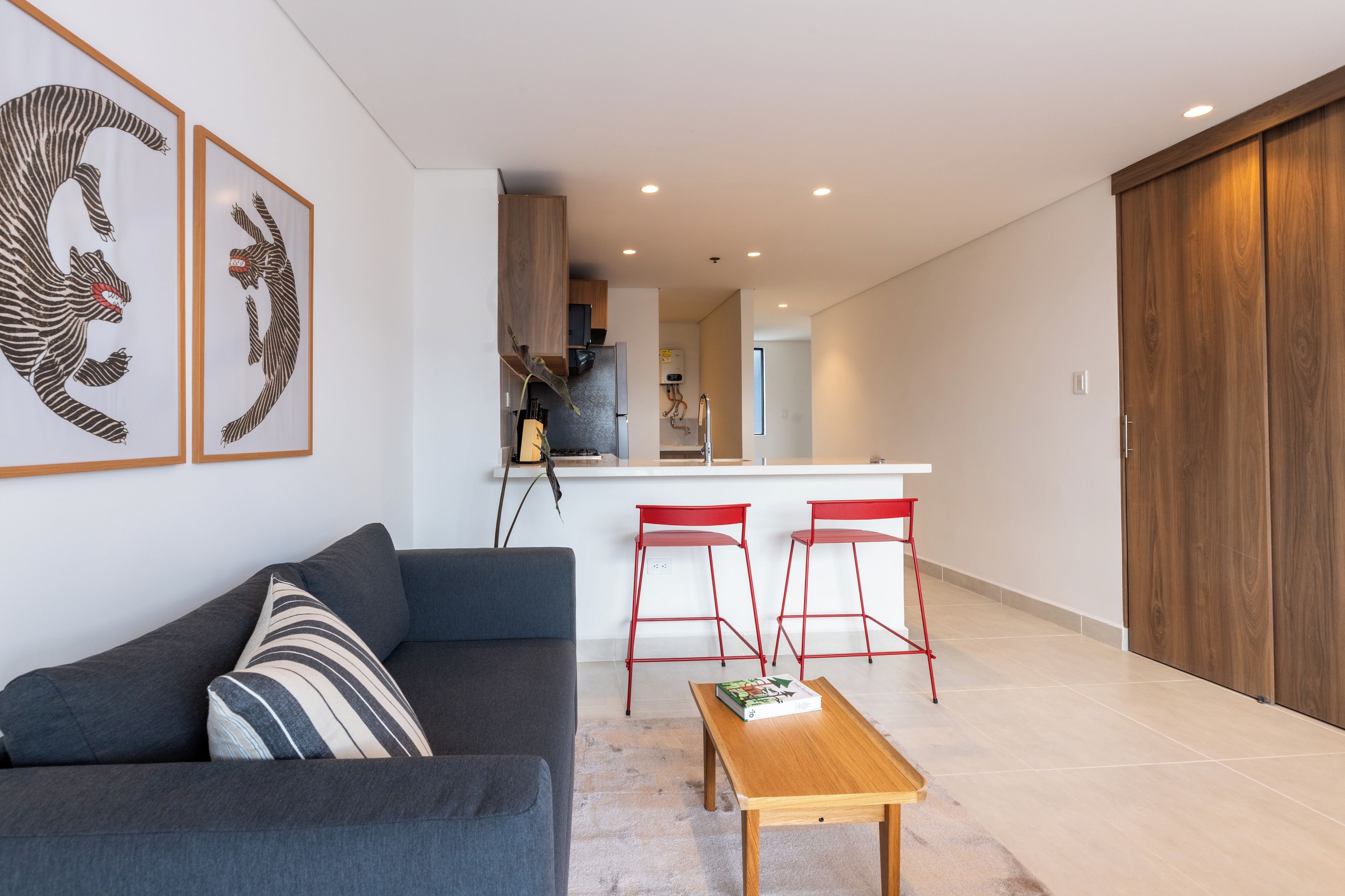 A modern living room with a sofa, a coffee table, and a kitchen area with a bar stool.