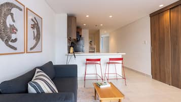 A modern living room with a sofa, a coffee table, and a kitchen area with a bar stool.