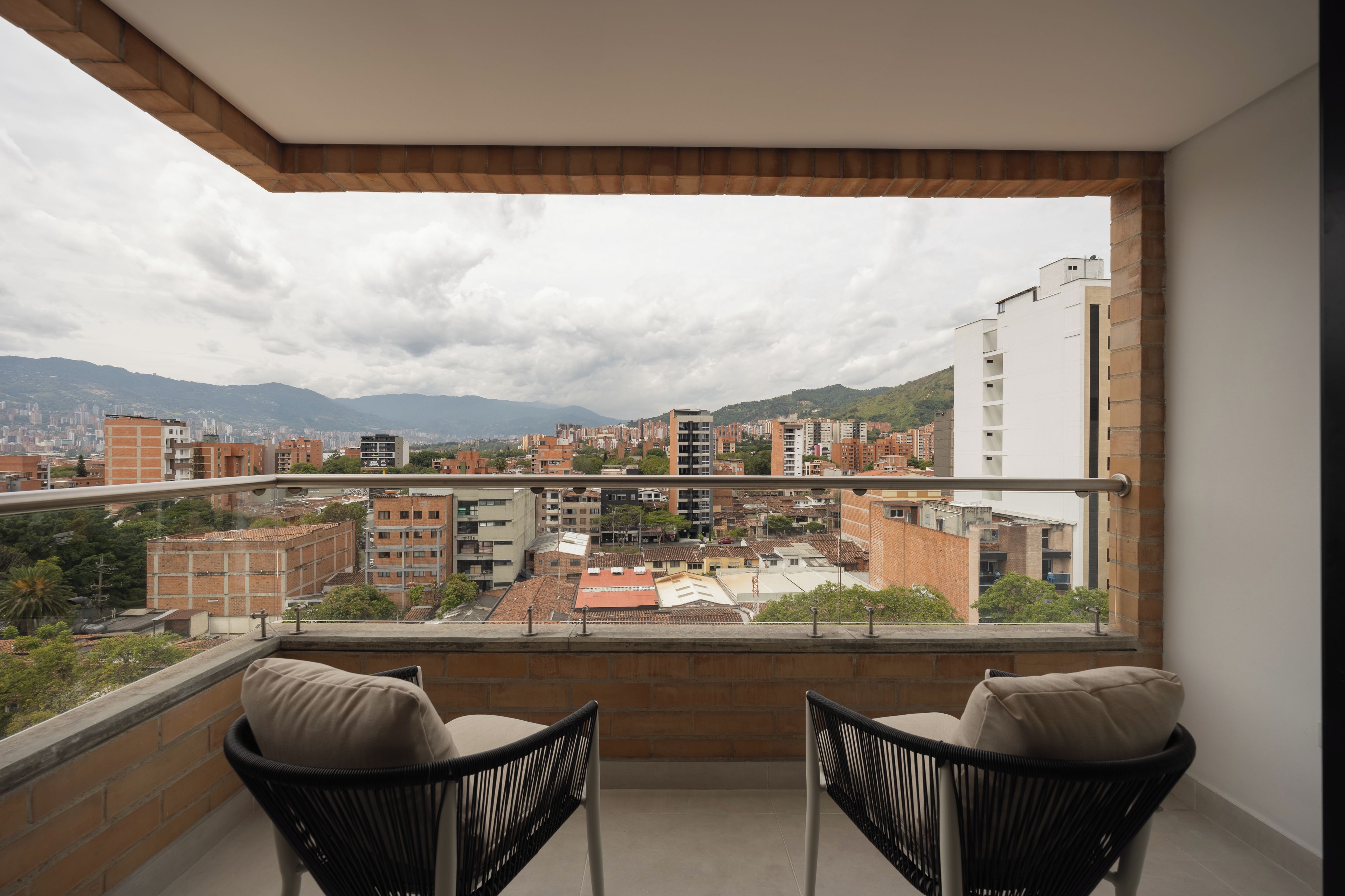 Ein Balkon mit zwei Stühlen und Blick auf eine Stadtlandschaft mit Gebäuden und Bergen in der Ferne.