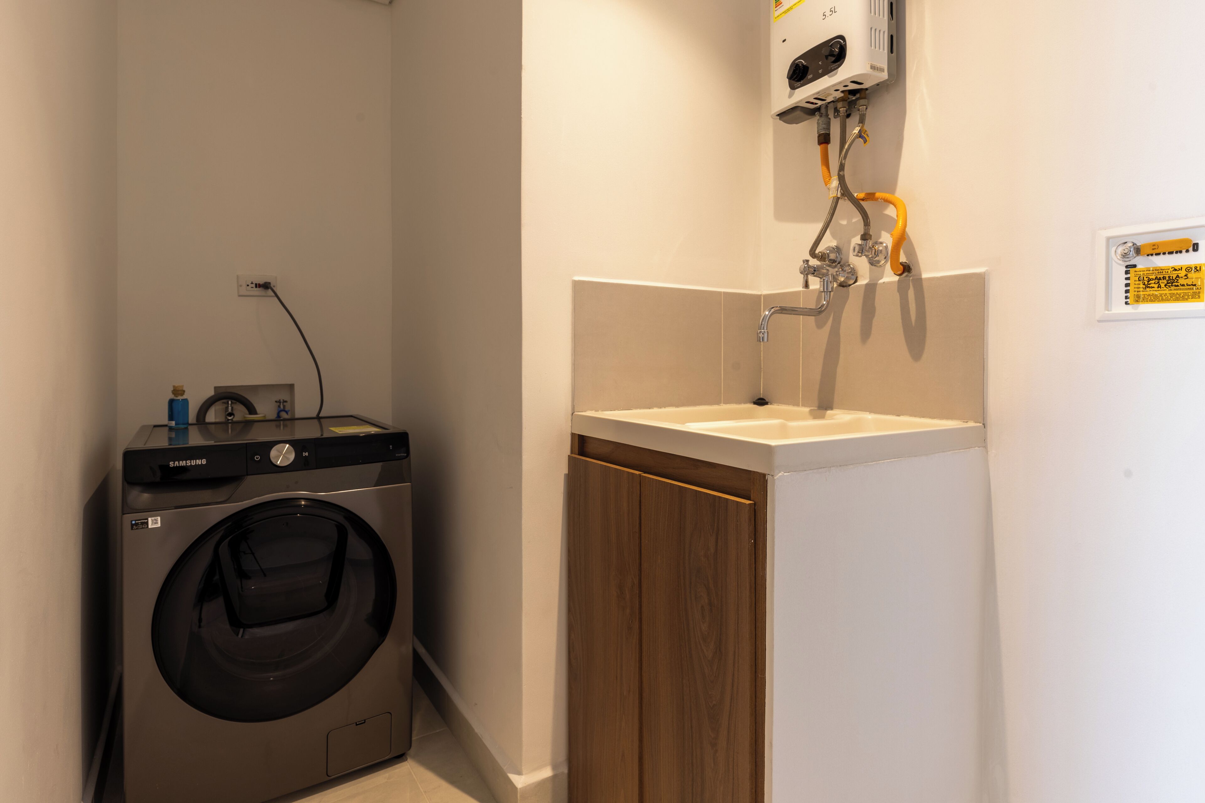 A compact laundry room with a washing machine, a sink, and a hose.