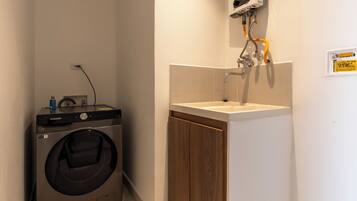 A compact laundry room with a washing machine, a sink, and a hose.
