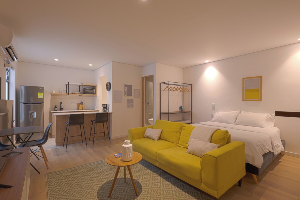 A compact living space with a kitchenette, a yellow sofa, a bed, and a small round table.