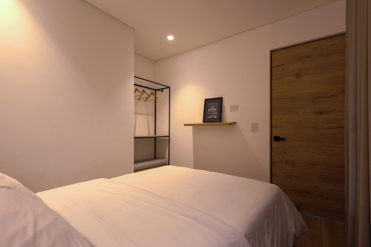 A bedroom with a bed, a wooden door, a wall-mounted shelf with a picture, and a clothing rack.