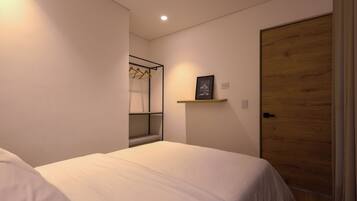 A bedroom with a bed, a wooden door, a wall-mounted shelf with a picture, and a clothing rack.