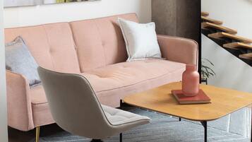 A modern living room with a pink sofa, a white chair, a wooden coffee table, and a large plant.