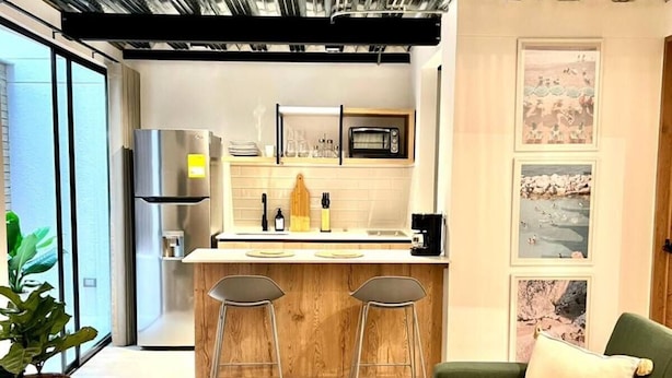 A modern kitchen with a central island, bar stools, and a green sofa in a living area. - VENTO MOLINO (BELEN)