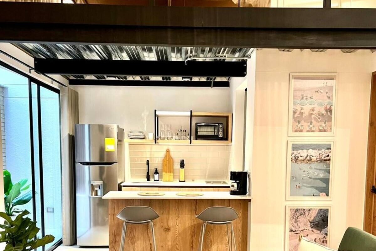 A modern kitchen with a central island, bar stools, and a green sofa in a living area.