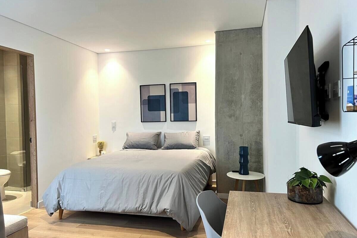 A modern bedroom with a bed, bedside table, and a TV mounted on the wall.