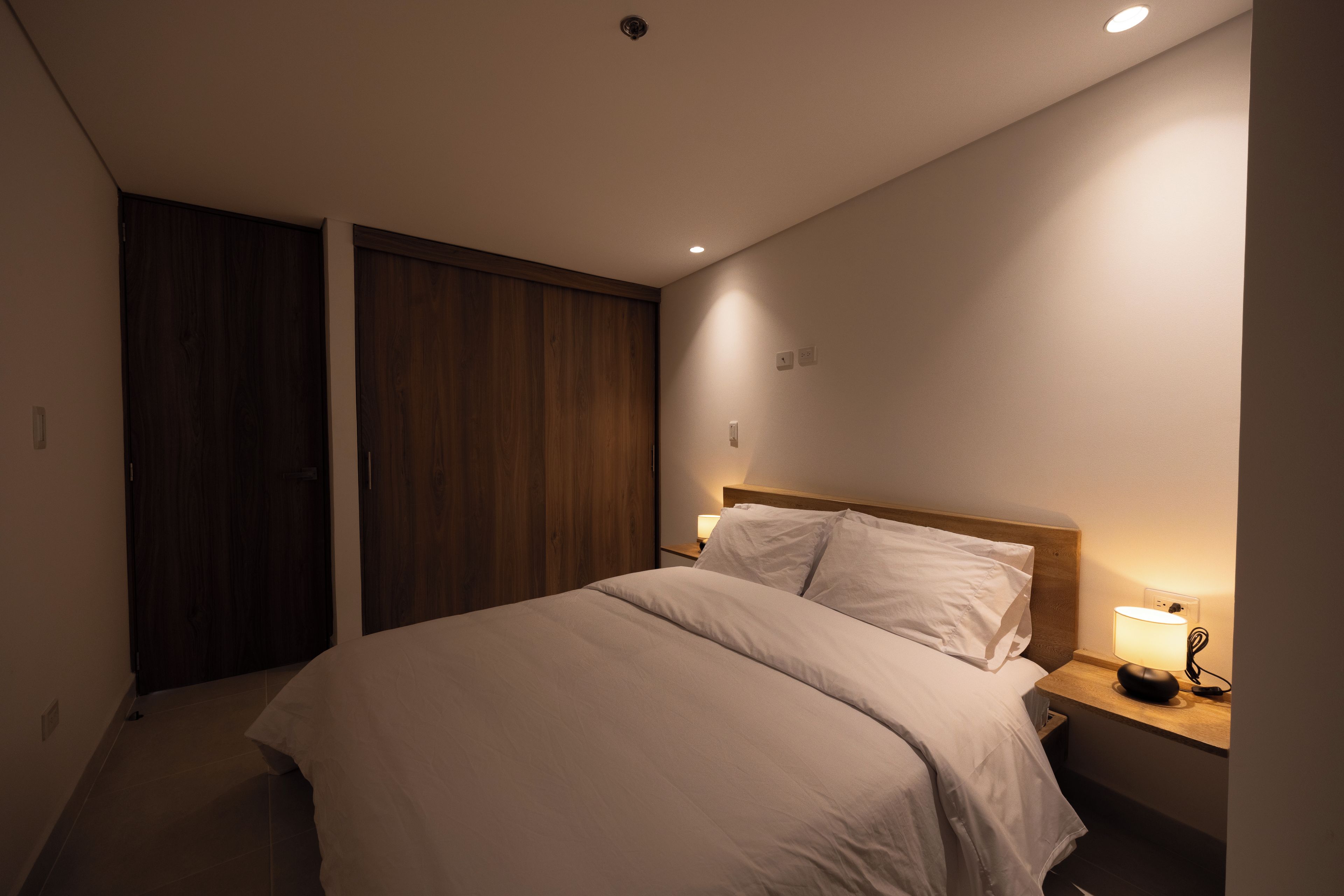Een slaapkamer met een bed, nachtkastjes, een kledingkast en een wandlamp.