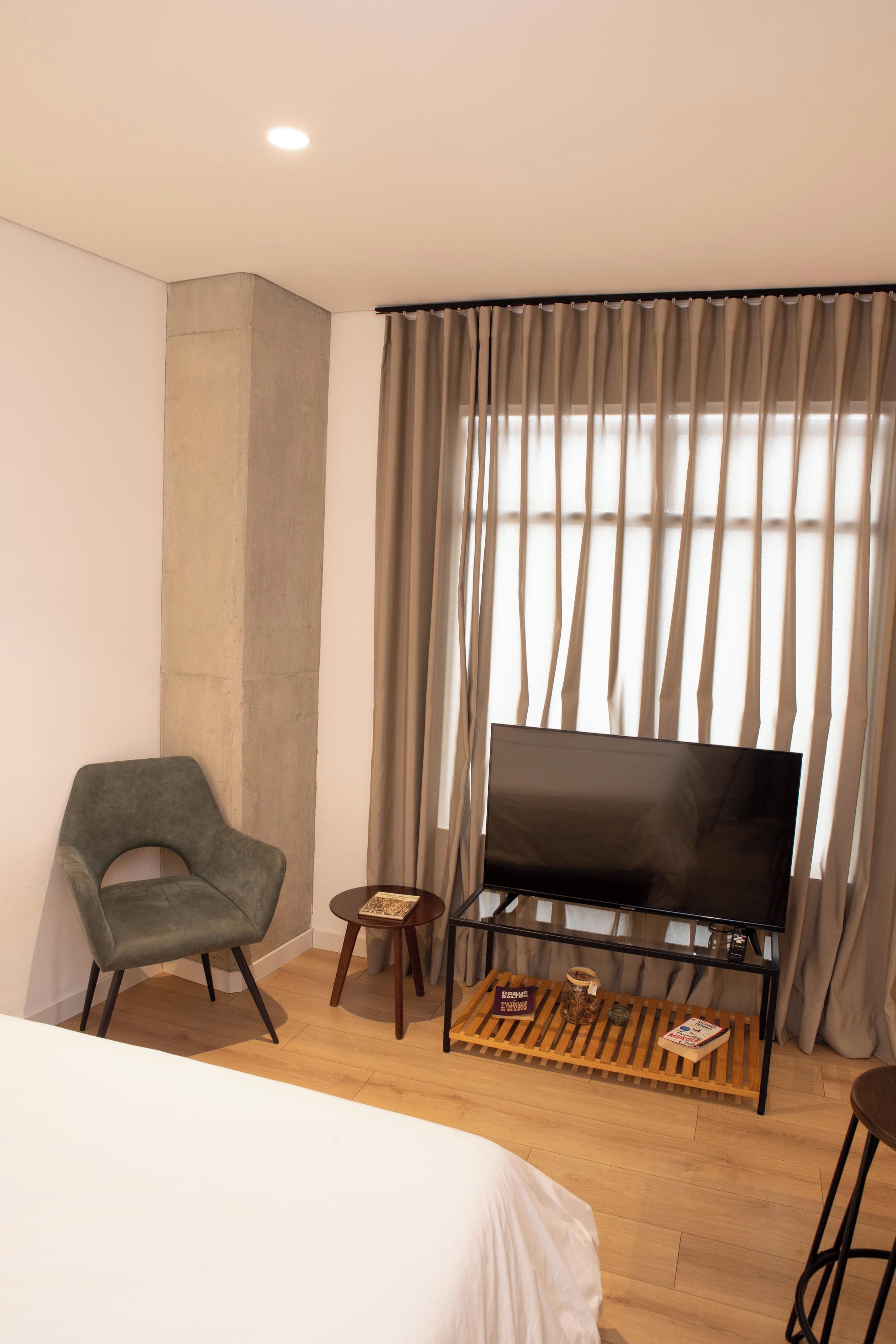 A hotel room with a bed, a television on a stand, a chair, a small table, and curtains.