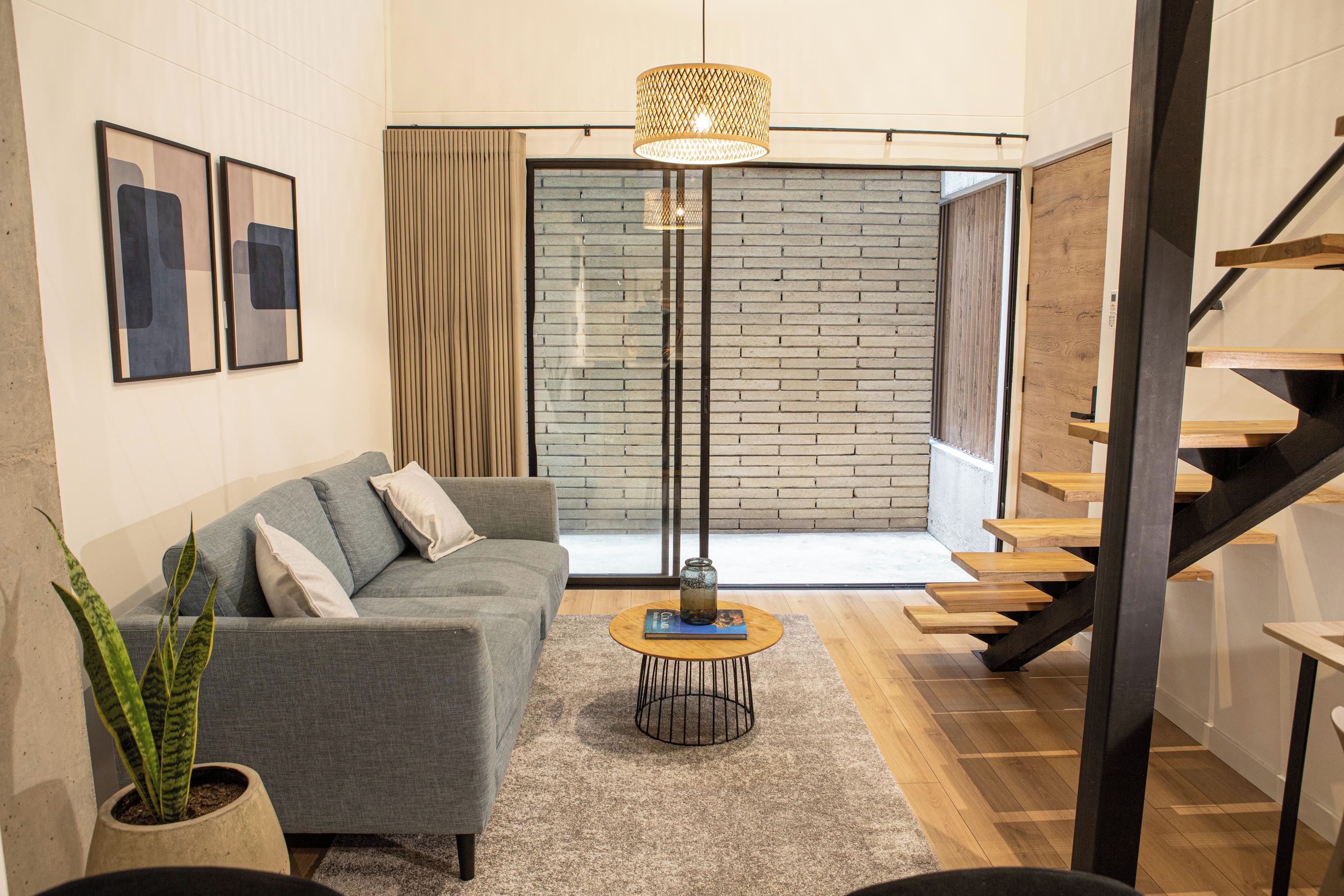 Un salon moderne avec un canapé gris, une table basse, une plante en pot et un escalier.