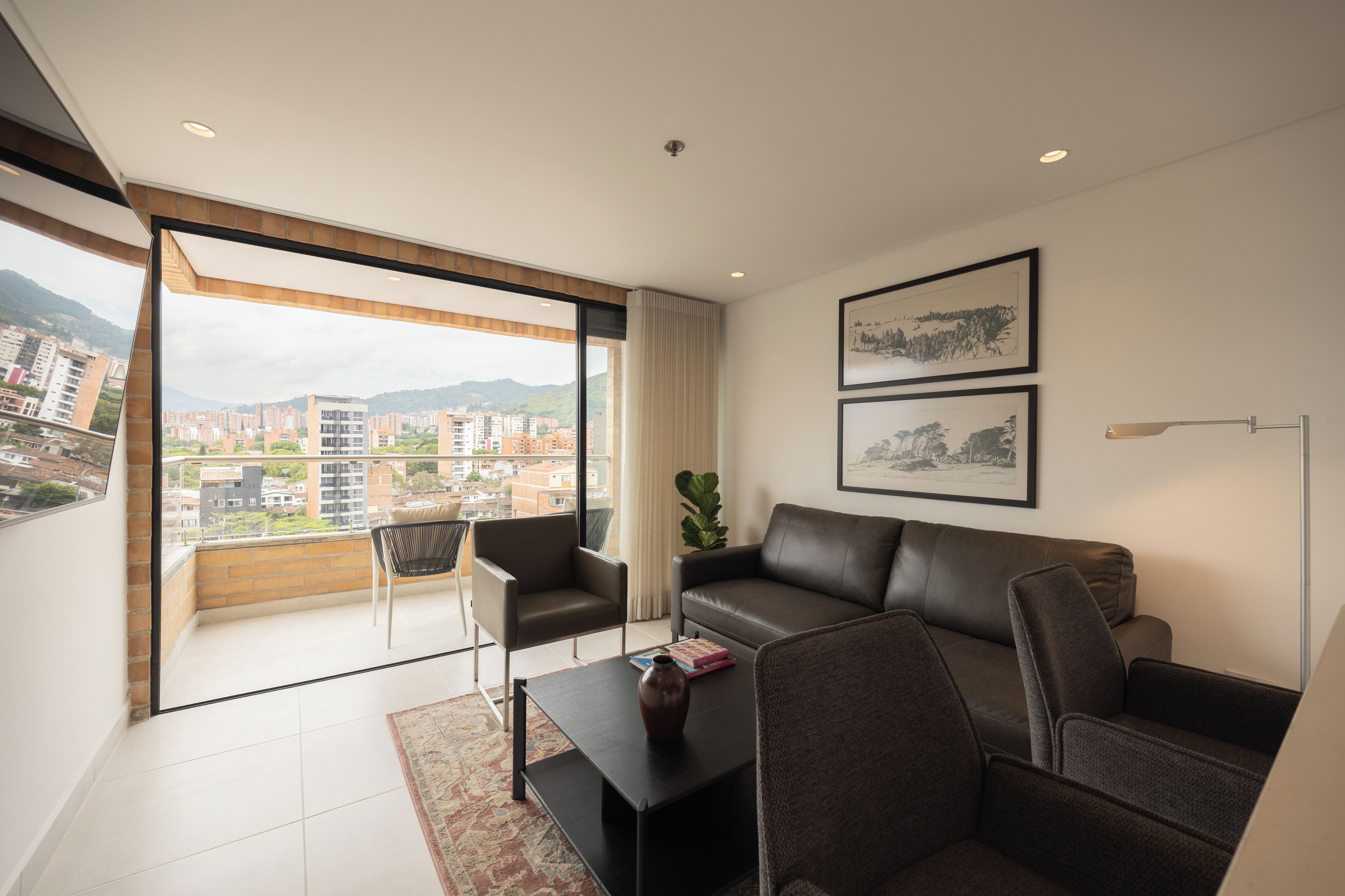 A modern living room with a leather sofa, a coffee table, and a view of a cityscape through large windows.