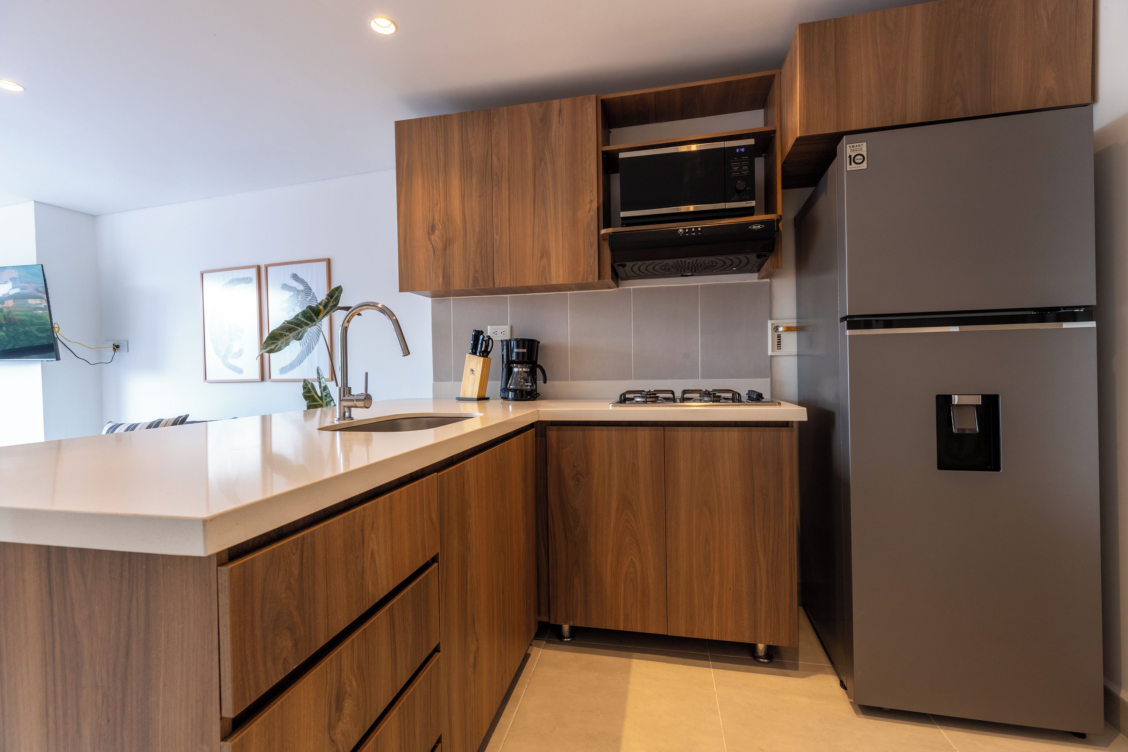 A modern kitchen with wooden cabinets, a stainless steel refrigerator, a built-in oven, and a coffee maker.