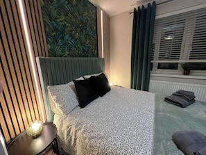 Un dormitorio moderno con cama, mesita de noche, lámpara de pared, ventana con cortinas y radiador.