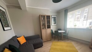 A living room with a sofa, a yellow rug, a cabinet, and a dining area with chairs. - Spacious & Modern Family Gem (London)