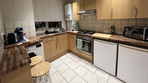 A modern kitchen with wooden cabinets, a built-in oven, a microwave, and a coffee machine. - Spacious & Modern Family Gem (London)