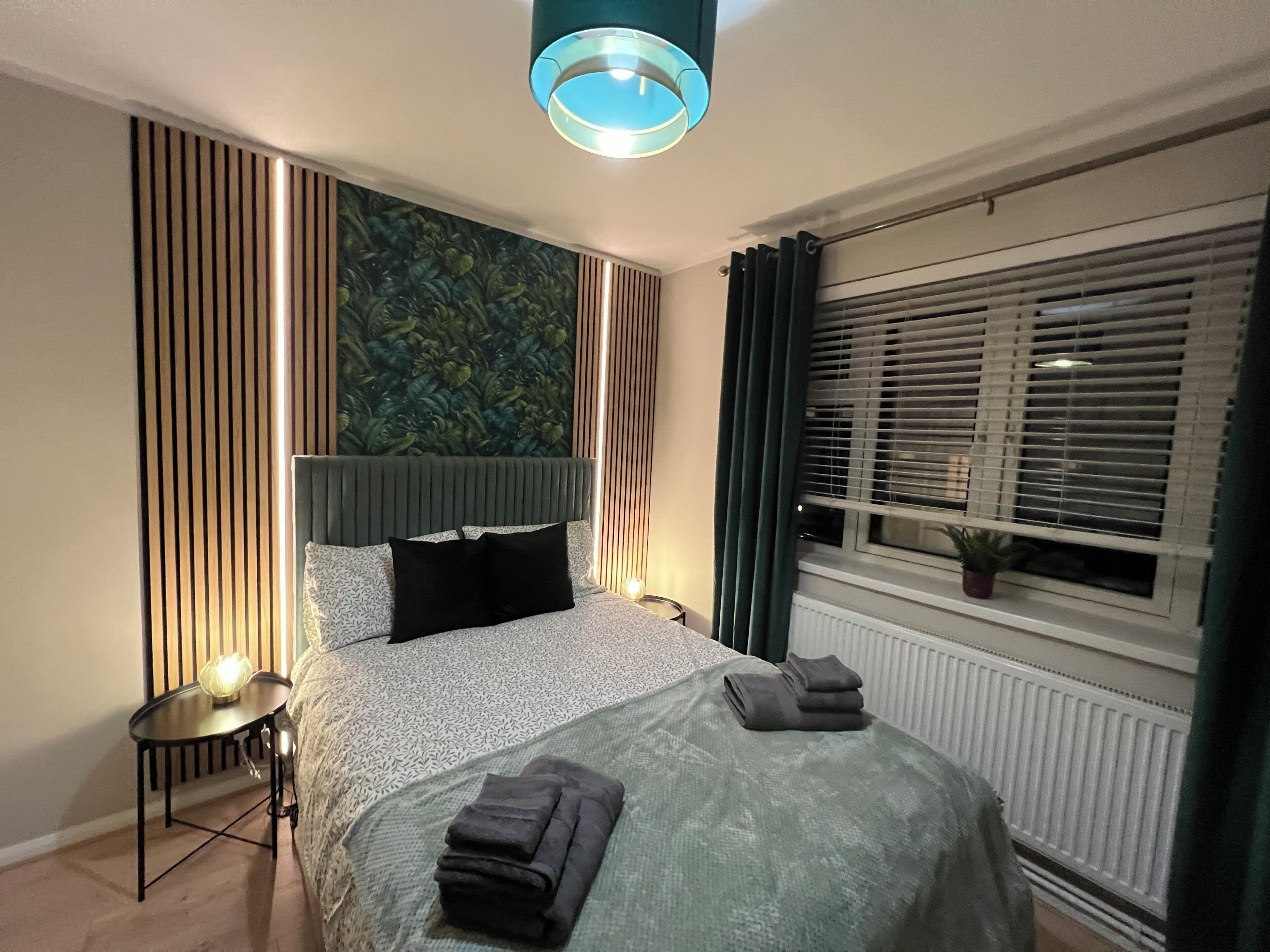 A modern bedroom with a bed, bedside table, and a window with blinds.